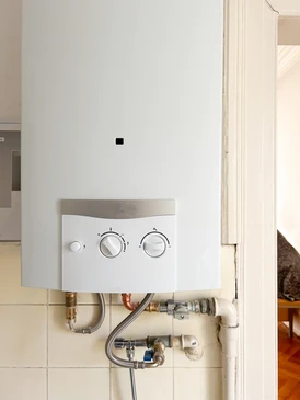 Plombier professionnel en salopette et casquette installant ou réparant un chauffe-eau électrique mural dans une salle de bain moderne