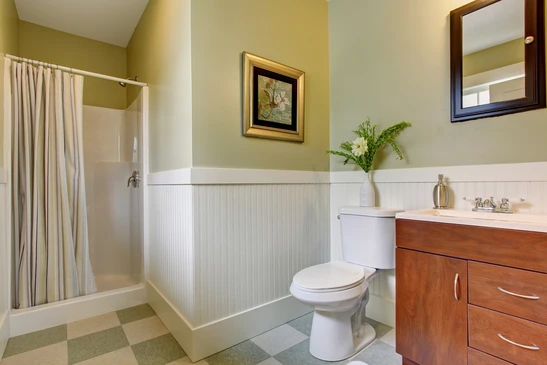 Salle de bain résidentielle avec baignoire-douche à rideau rayé, toilette blanche standard, vanité en bois avec comptoir stratifié et lavabo intégré