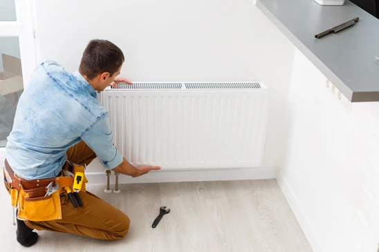 Un plombier-chauffagiste installe un radiateur à panneaux dans une maison moderne